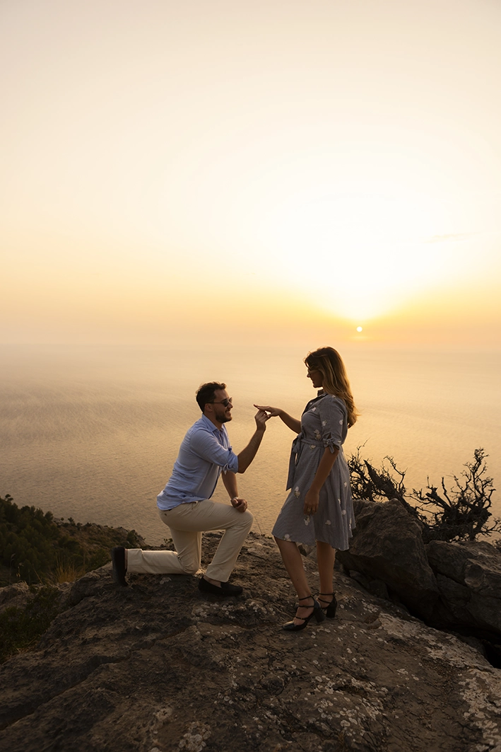 Sunset proposal with Lucas kneeling before Rafa on a Mallorca cliff.