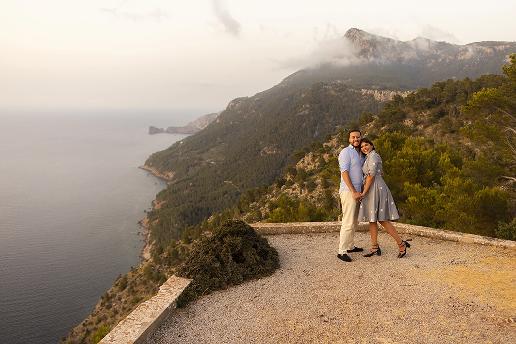 Couple smiling and embracing at a viewpoint with stunning coastal views in Mallorca after the proposal.