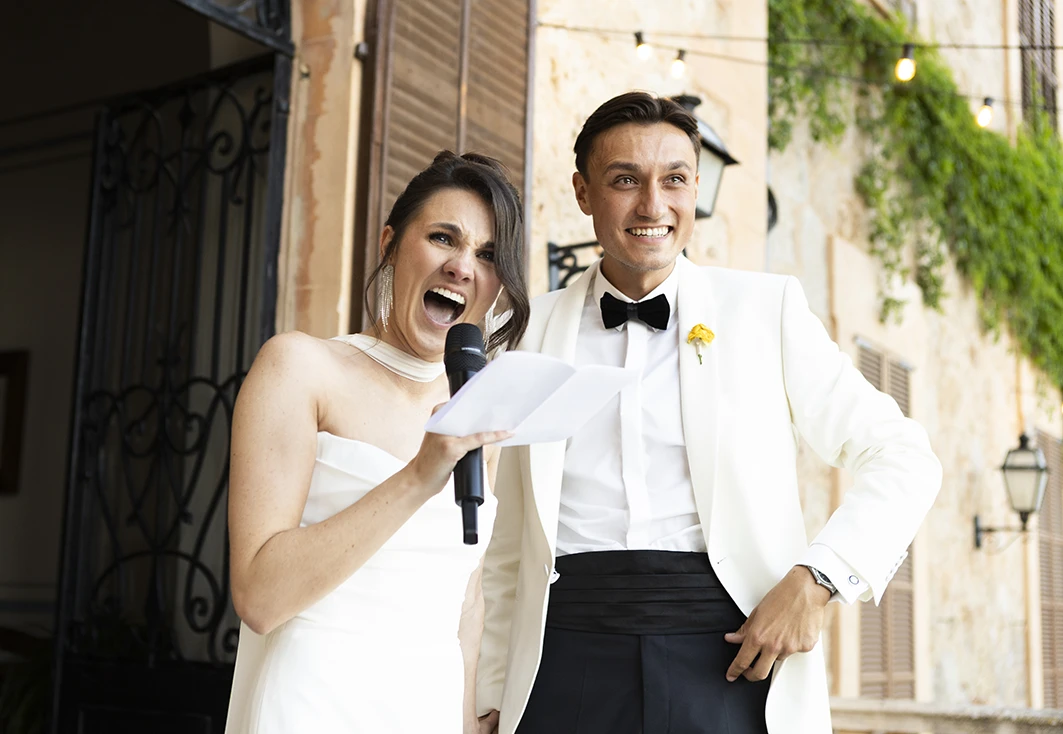 Bride laughing heartily while holding a microphone next to the groom at Finca Son Togores, Mallorca.