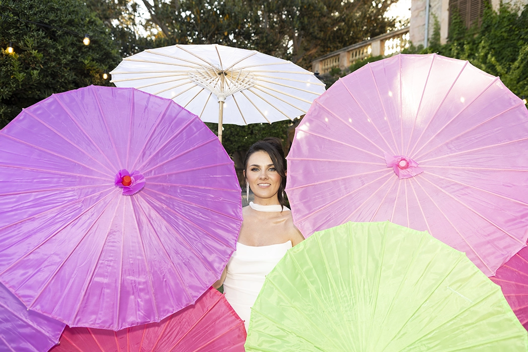 The bride smiles surrounded by large, vibrant-colored parasols.