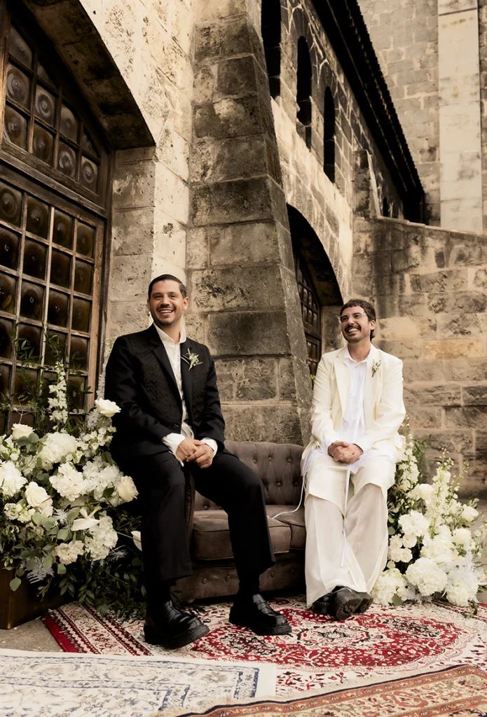 Grooms sitting together surrounded by flowers during their wedding at Finca Gordiola, Mallorca.