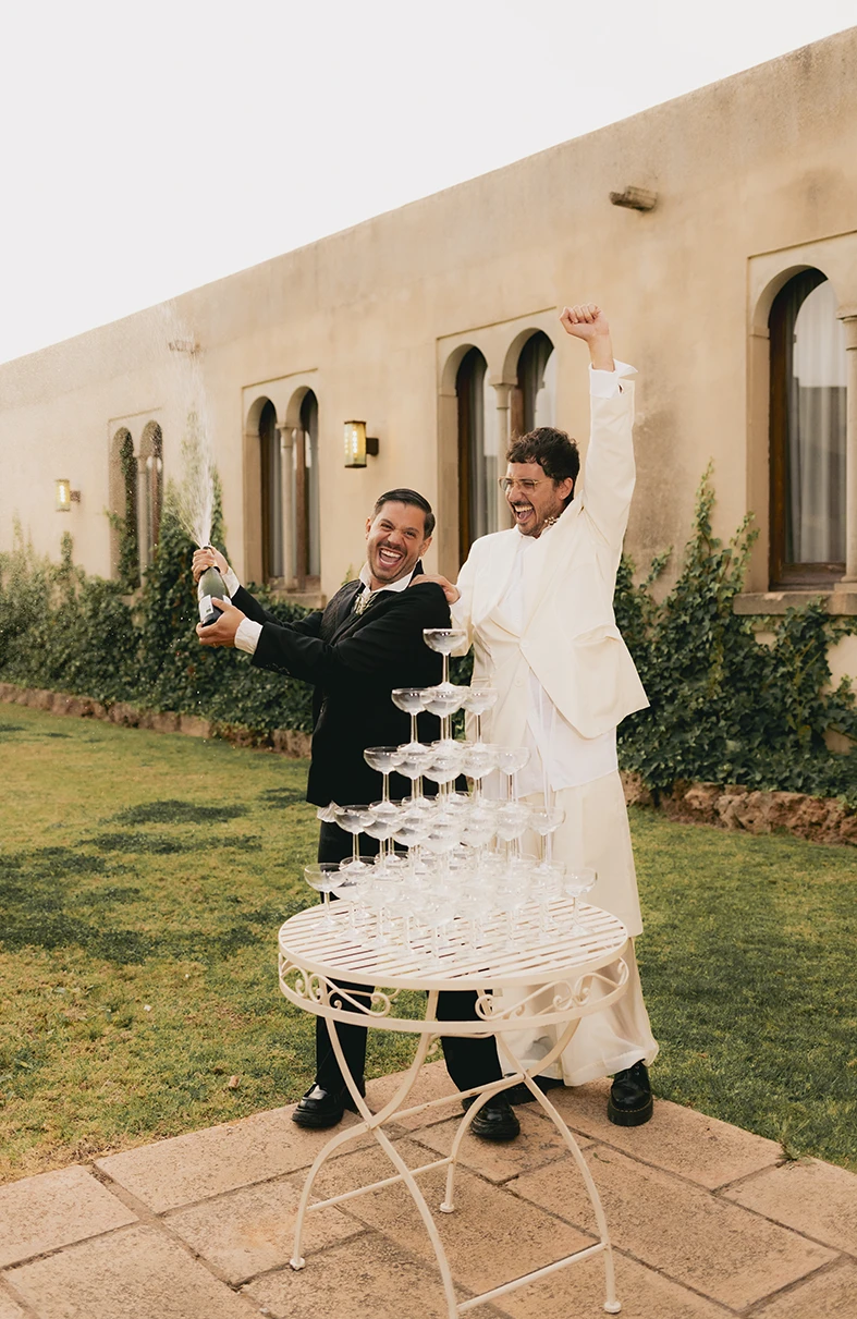 Grooms Jon and Santi popping champagne during their wedding celebration at Finca Gordiola Mallorca.