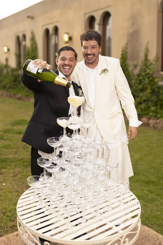Jon and Santi pouring champagne together into a glass tower at their wedding at Finca Gordiola.