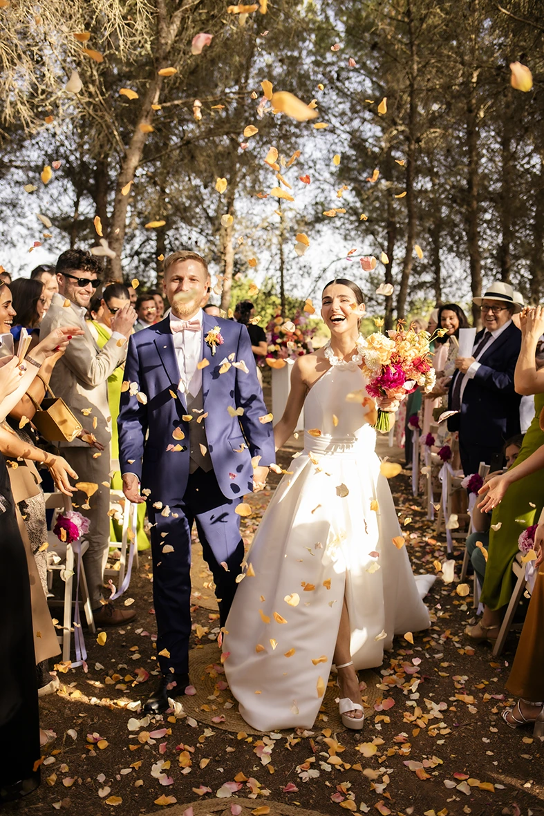 Bride and groom walking down the aisle under a shower of flower petals at their outdoor wedding ceremony in Mallorca.