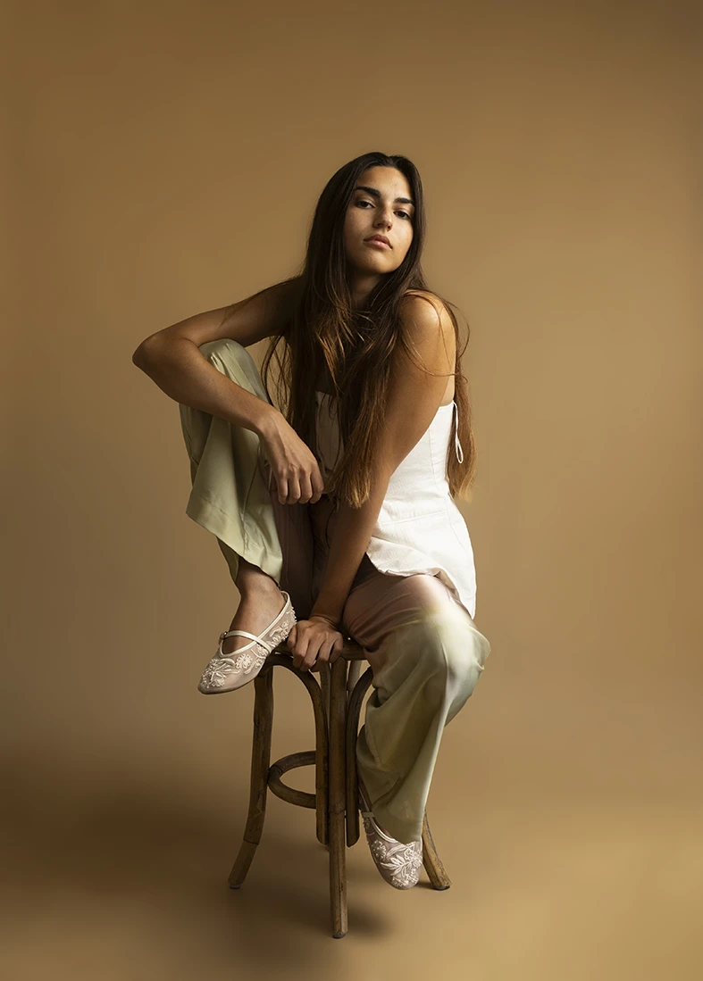 Modelo sentada de forma relajada sobre un taburete, con mirada al frente y fondo neutro. Cómo puedes ser modelo en Mallorca. Foto de Inma del Valle.