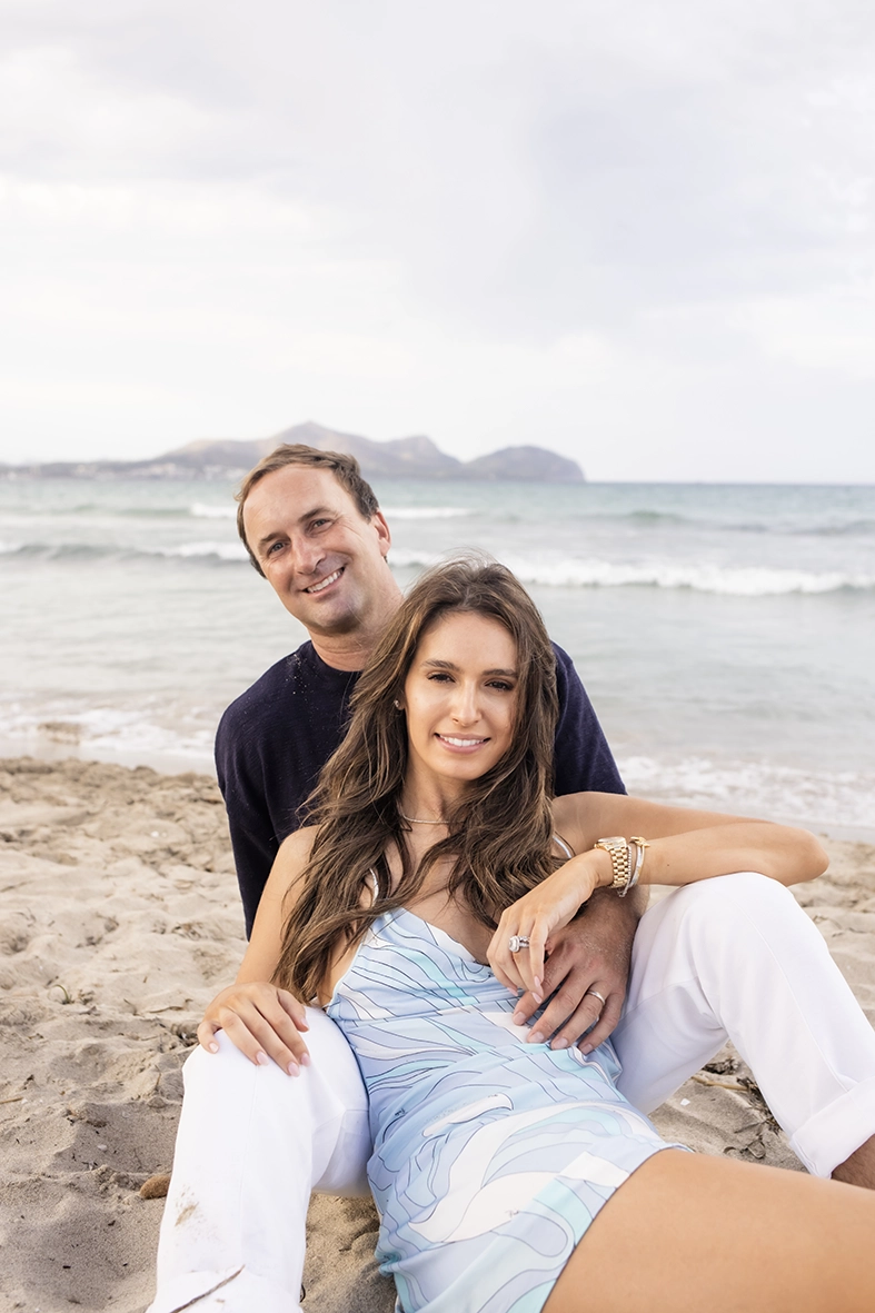 Family photo session in Mallorca by Inma del Valle, couple sitting on the sand in a relaxed pose by the sea.
