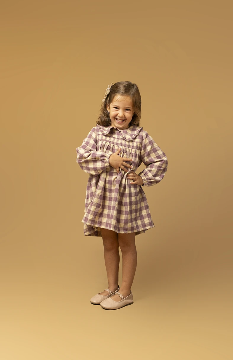 Niña sonriendo con vestido de cuadros. Fotógrafo de niños para agencia en Mallorca.