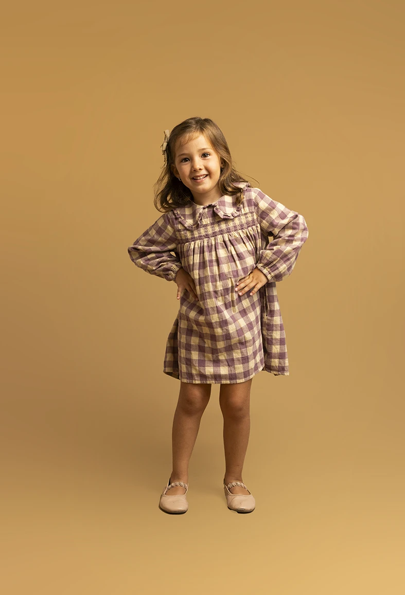 Niña con vestido de cuadros y manos en la cintura. Fotógrafo de niños para agencia en Mallorca.