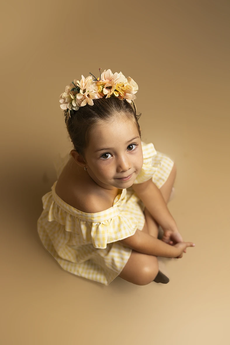 Niña sentada con vestido amarillo y corona de flores. Fotógrafo de niños para agencia en Mallorca.