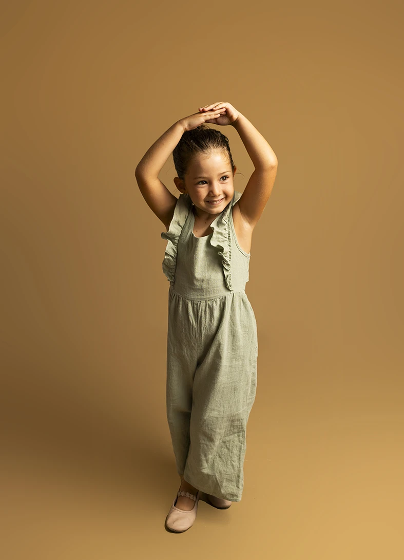 Niña con mono verde y brazos arriba. Fotógrafo de niños para agencia en Mallorca.