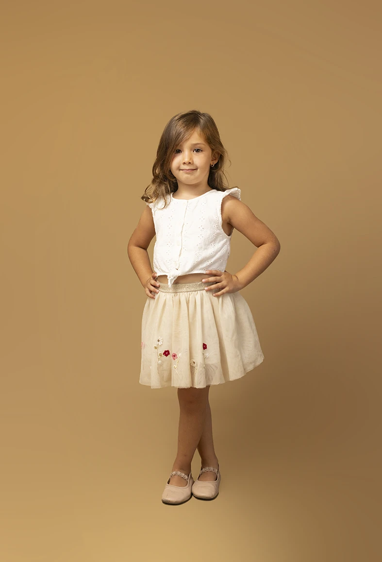 Niña con falda beige posando con seguridad. Fotógrafo de niños para agencia en Mallorca.