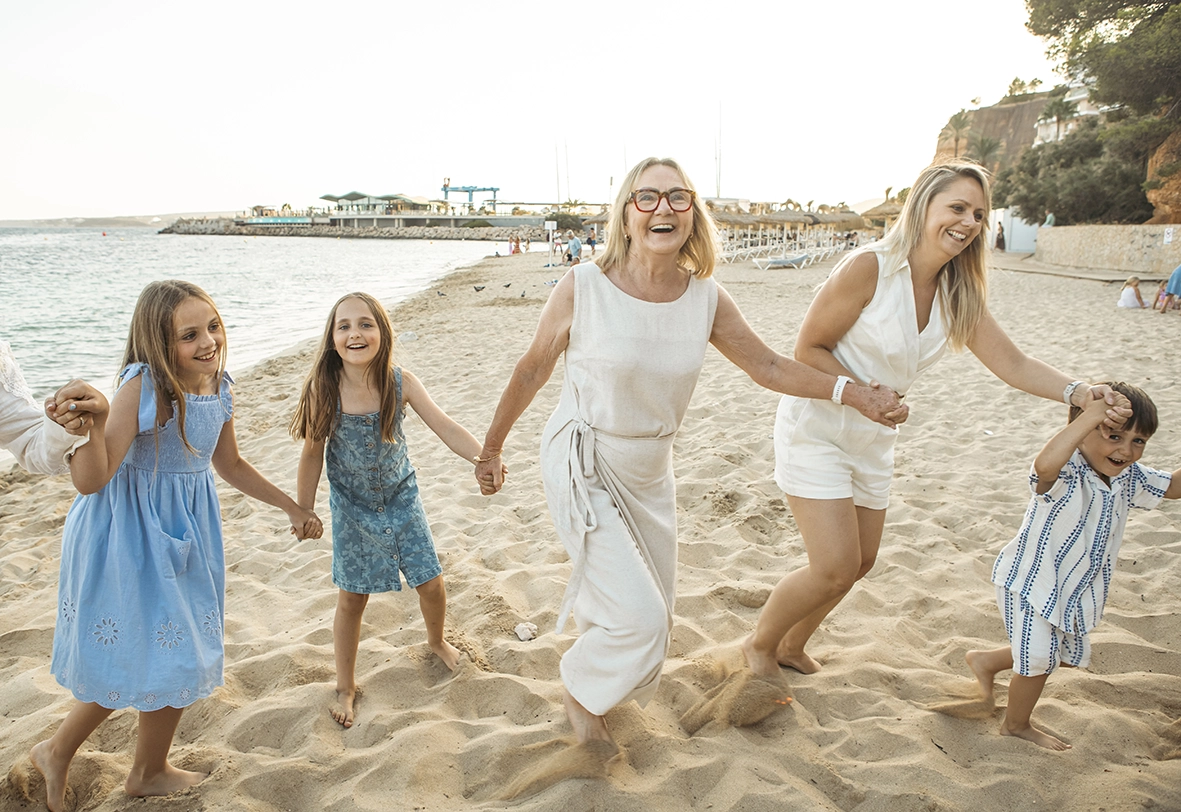 Abuela y nietas caminando de la mano en la playa con fotógrafo familiar en Mallorca. Foto de Inma del Valle.