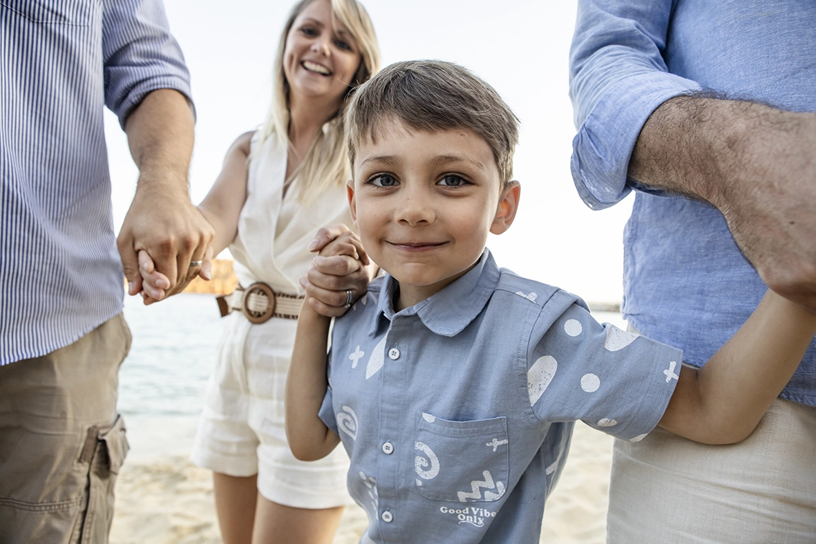Niño sonriente tomado de la mano de su familia en una sesión con fotógrafo familiar en Mallorca. Imagen de Inma del Valle.