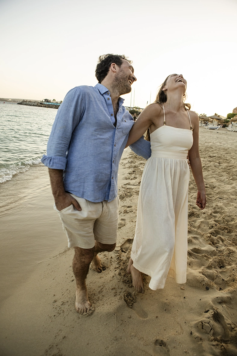 Pareja riendo mientras camina por la orilla, captada por fotógrafo familiar en Mallorca, Inma del Valle.