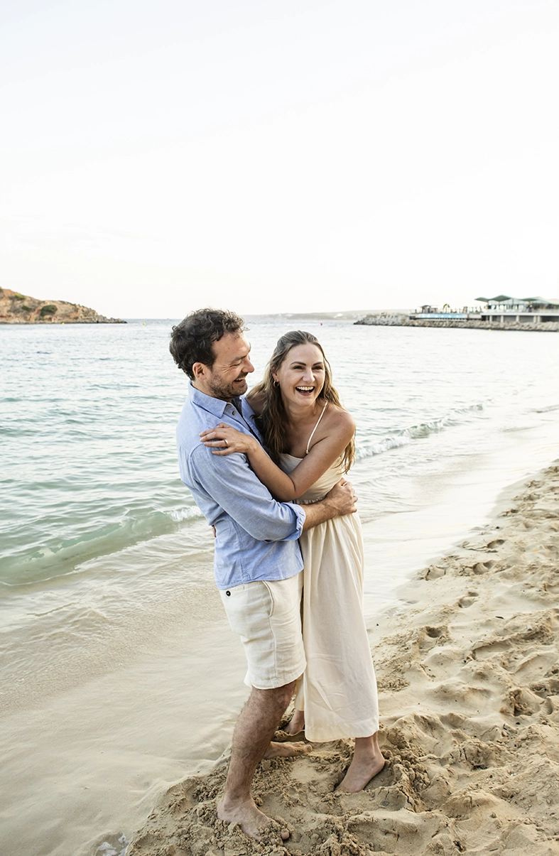 Pareja sonriendo y abrazándose en la playa durante una sesión con fotógrafo familiar en Mallorca, Inma del Valle.