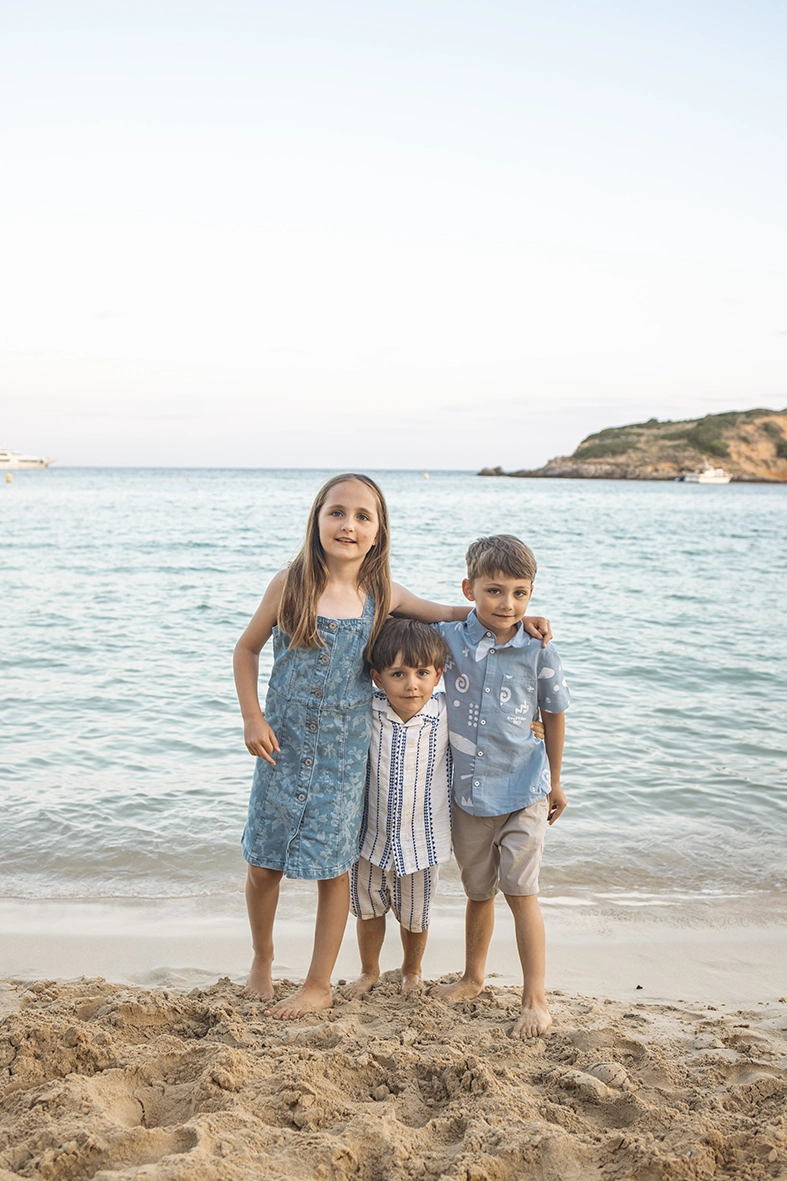 Tres niños pequeños abrazados frente al mar durante una sesión de fotos familiar en la playa con Inma del Valle, fotógrafo familiar en Mallorca.