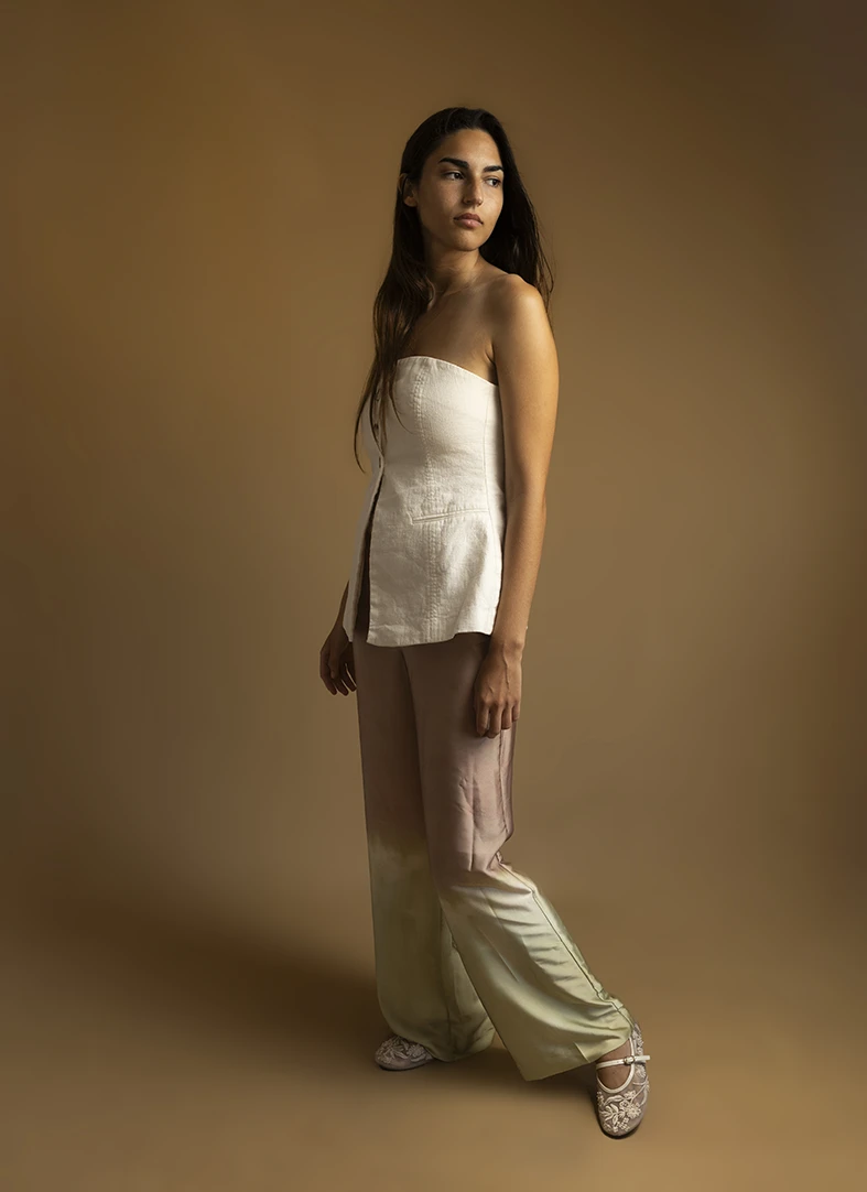 Model standing in studio with beige background, wearing a white strapless top and flowy pants. How you can become a model in Mallorca. Photo by Inma del Valle.