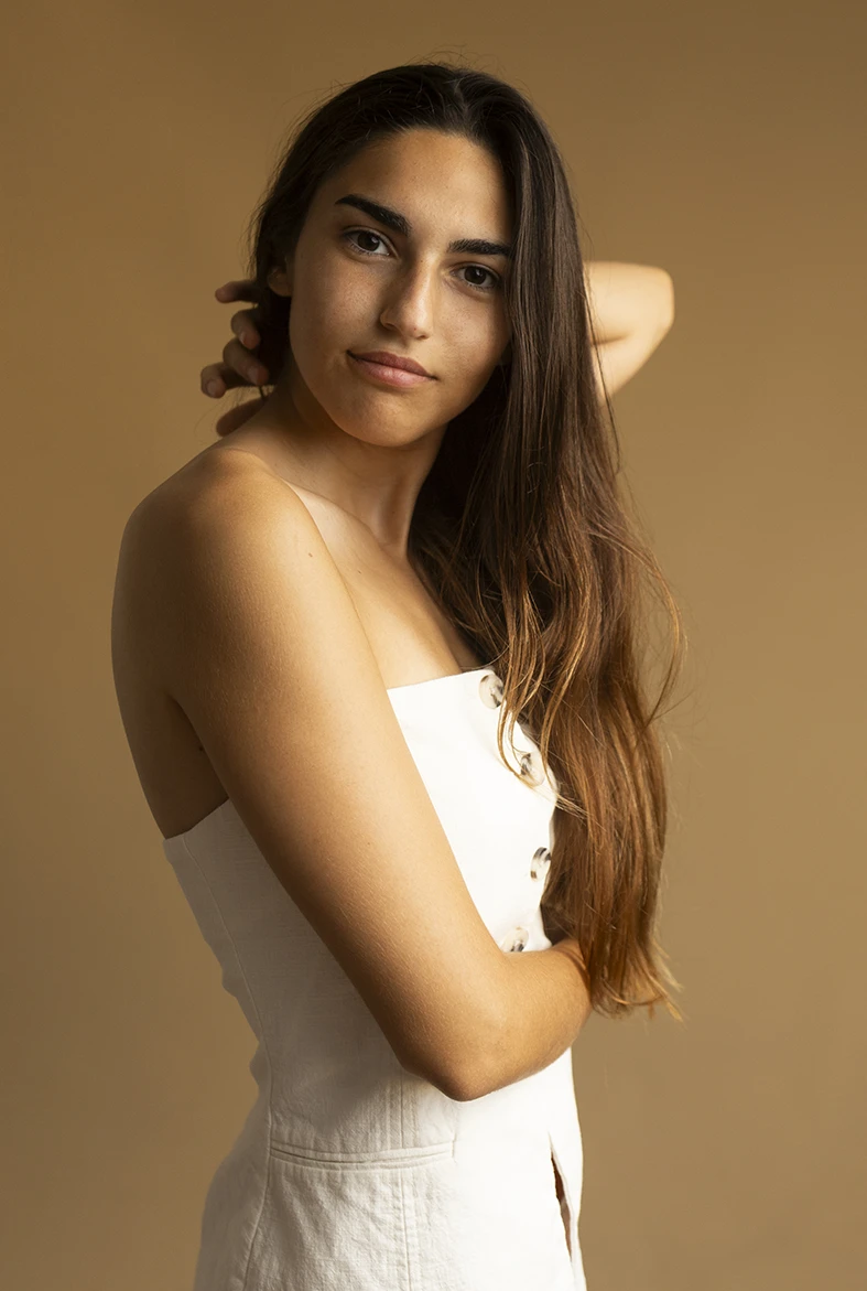 Medium shot of model in white dress, hand on neck, soft expression. How you can become a model in Mallorca. Photo by Inma del Valle.