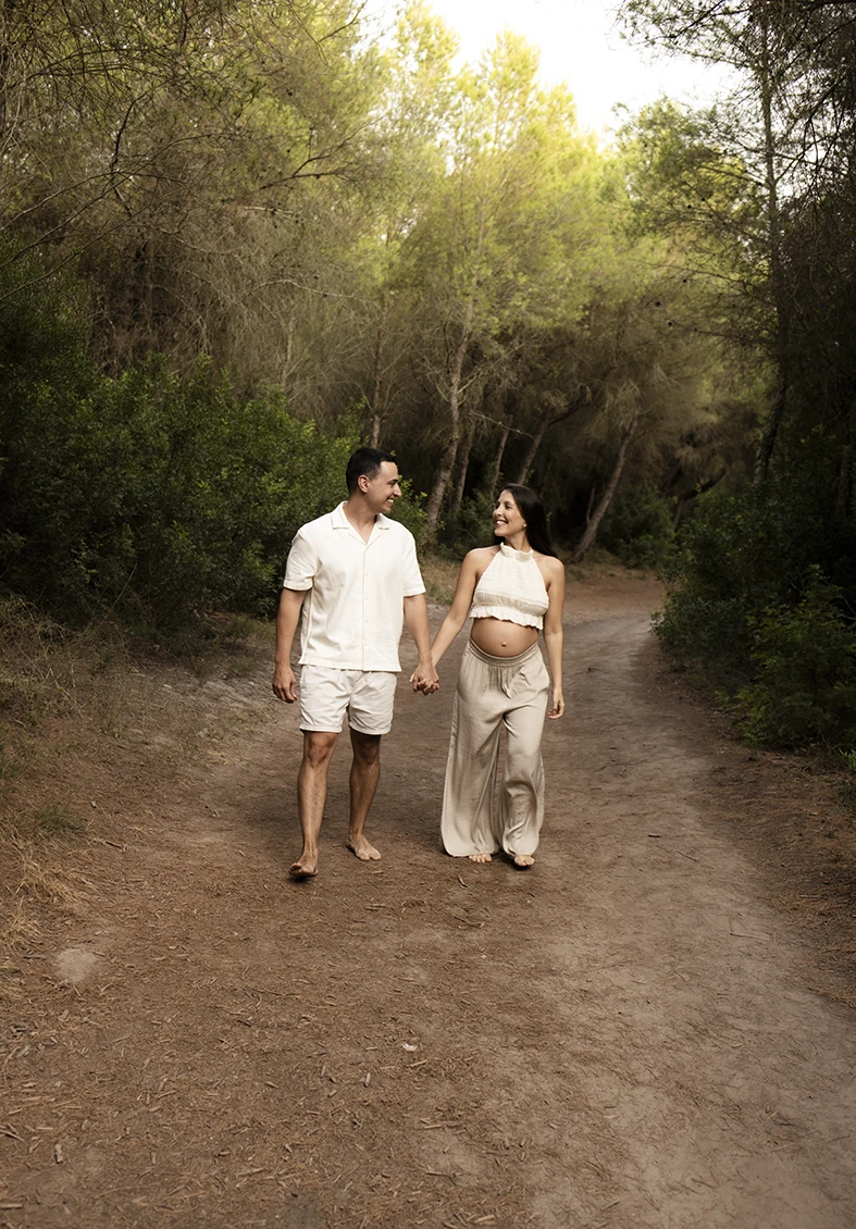 Pregnant couple walking hand in hand through a forest in Mallorca during a photo session.