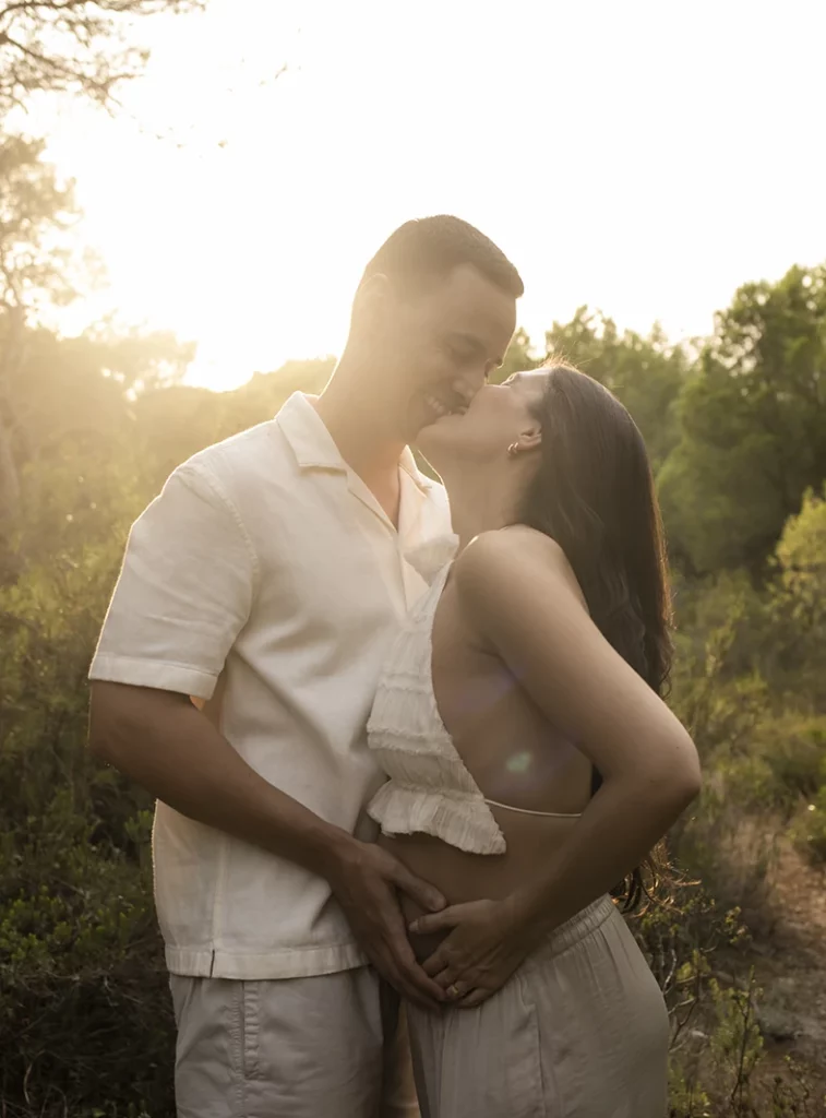 Pregnant couple kissing on a forest path in Mallorca during a sunset photo shoot.