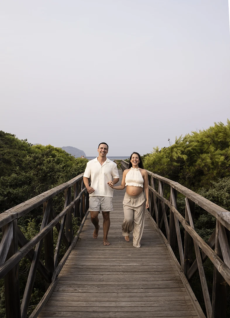 Pregnant couple walking hand in hand on a wooden bridge in Mallorca during their photo shoot.