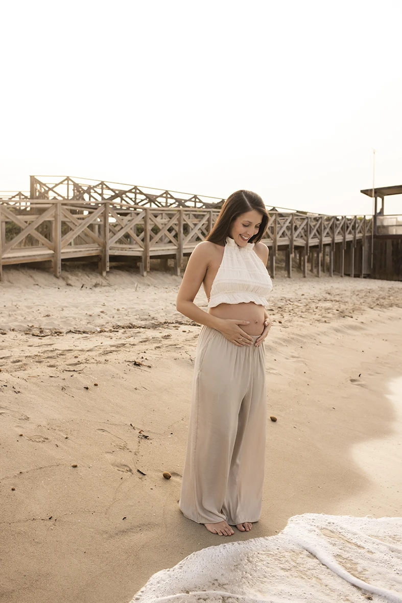 Pregnant woman caressing her baby bump on the beach shore in Mallorca during a photo shoot.