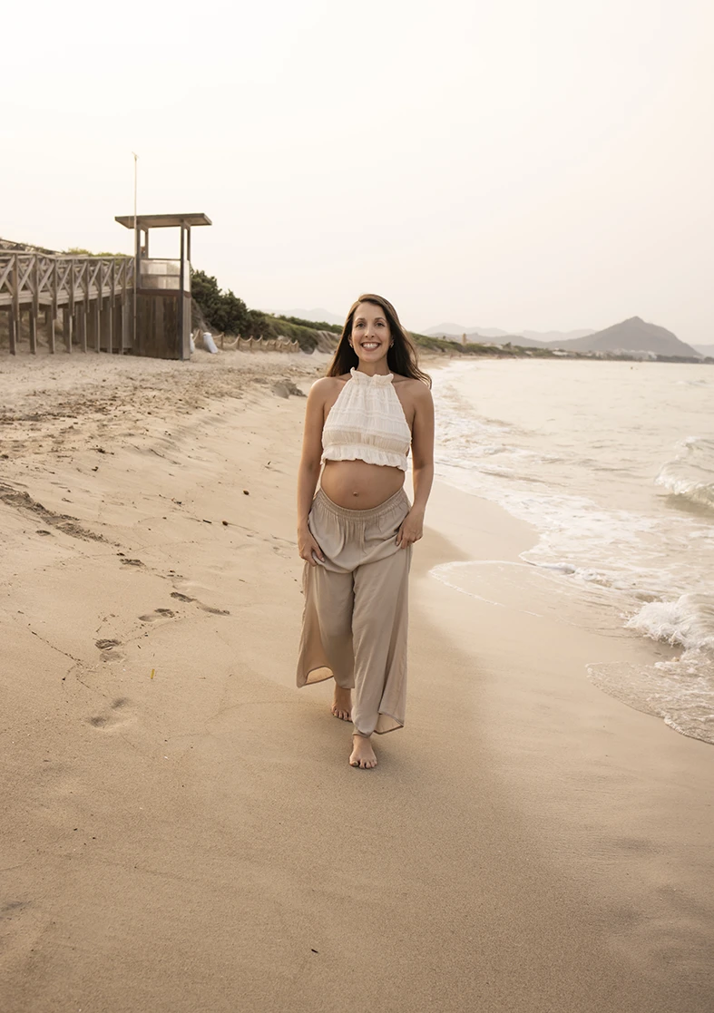 Pregnant woman walking barefoot along the beach shore in Mallorca during a photo shoot.
