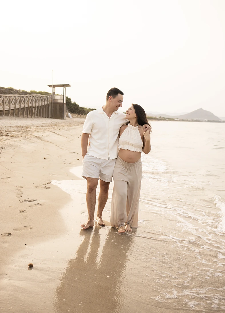 Pregnant couple walking together along the beach shore in Mallorca during their photo shoot.