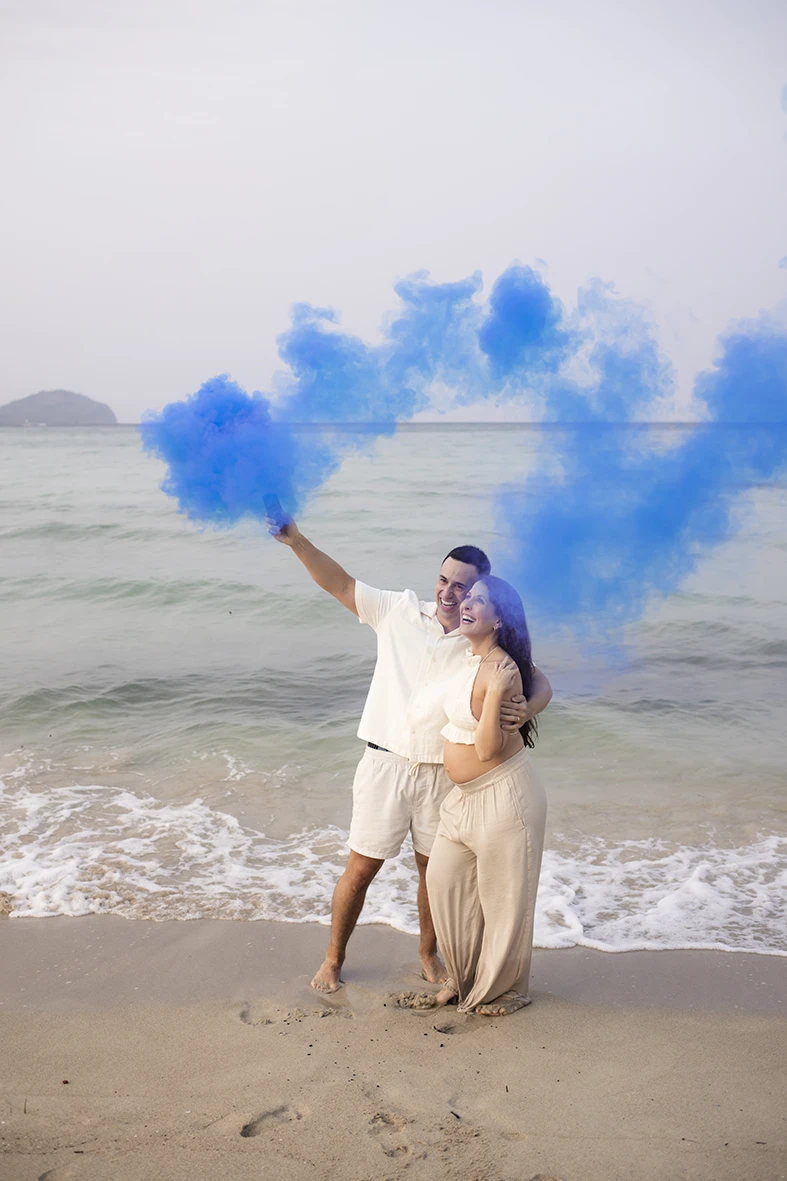 Pregnant couple celebrating on the beach in Mallorca with a blue smoke flare to reveal their baby’s gender.