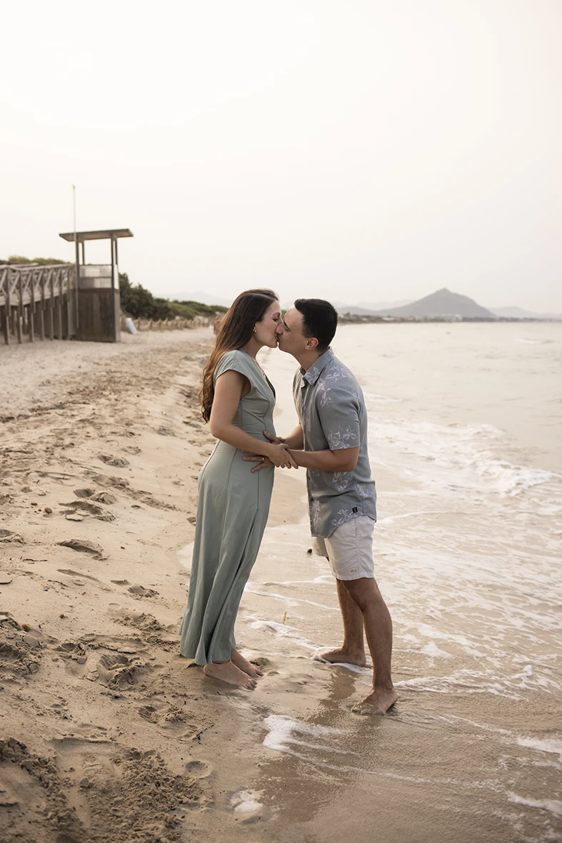 Pregnant couple kissing on the beach shore in Mallorca during their maternity photo shoot.