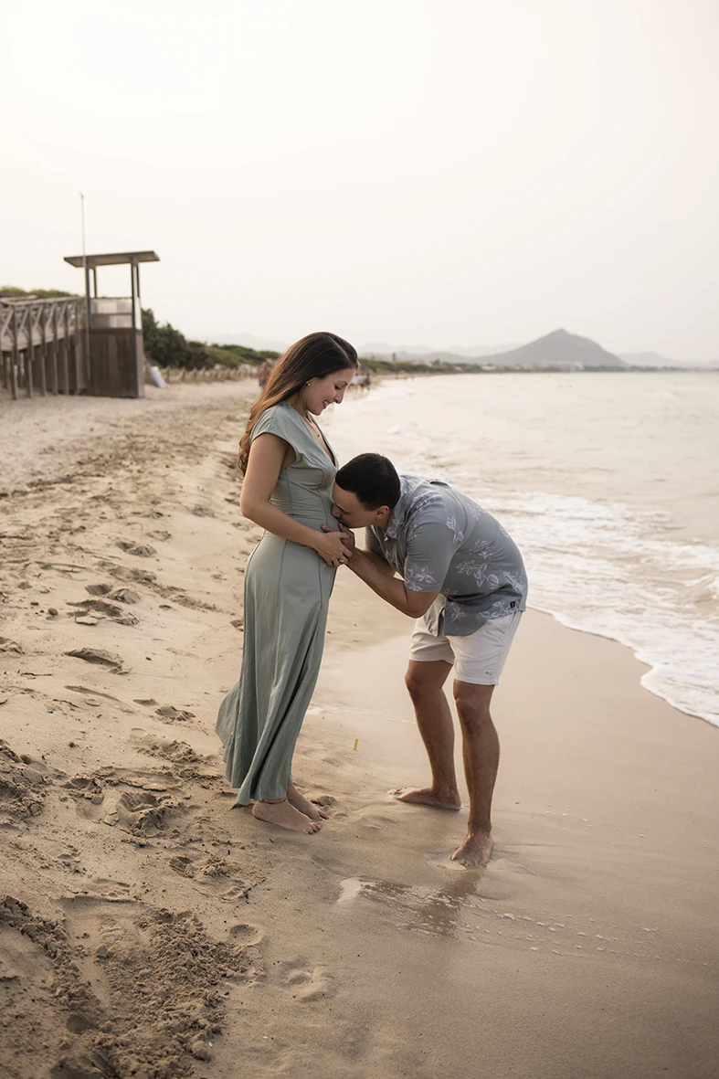 Man kissing his pregnant partner’s belly on the beach shore in Mallorca.