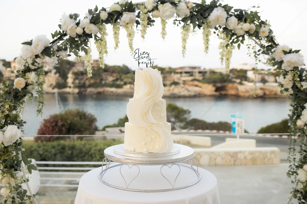 Elegant white wedding cake with floral decoration and sea view in Mallorca.