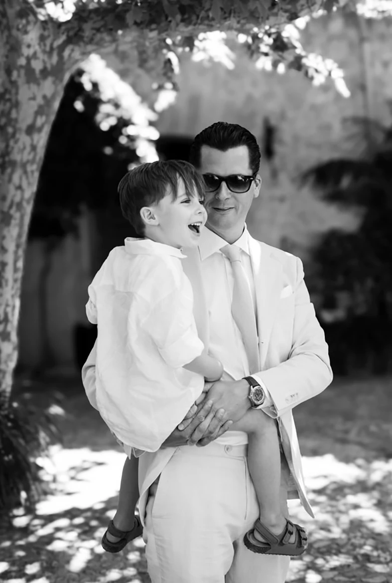 Man in a light suit holding a smiling child during a wedding in Mallorca.