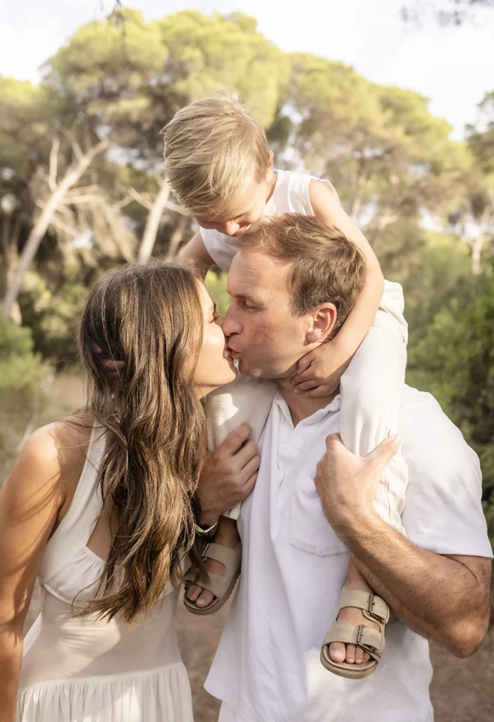 Sesión de fotos a familia en Mallorca realizada por Inma del Valle, pareja besándose con su hijo sobre los hombros en un entorno natural.