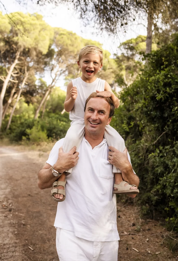 Sesión de fotos a familia en Mallorca realizada por Inma del Valle, padre con su hijo sobre los hombros caminando por un sendero del bosque.