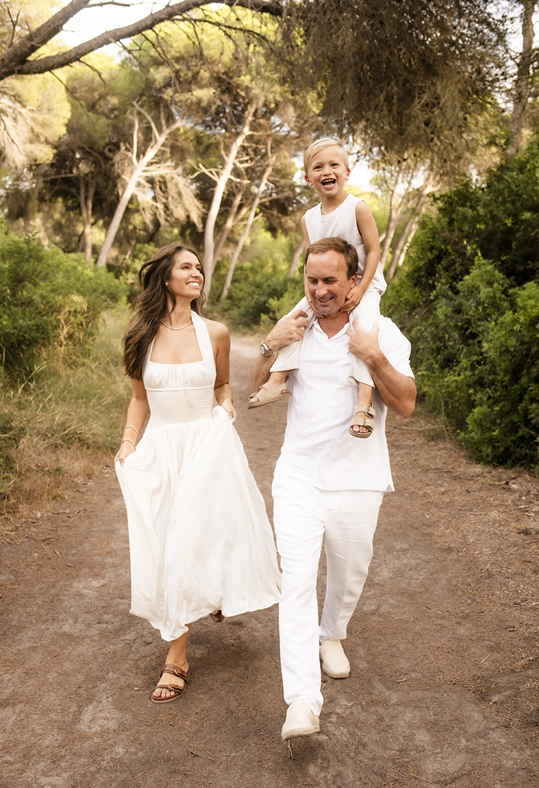 Sesión de fotos a familia en Mallorca realizada por Inma del Valle, padres caminando con su hijo sobre los hombros en un sendero natural.