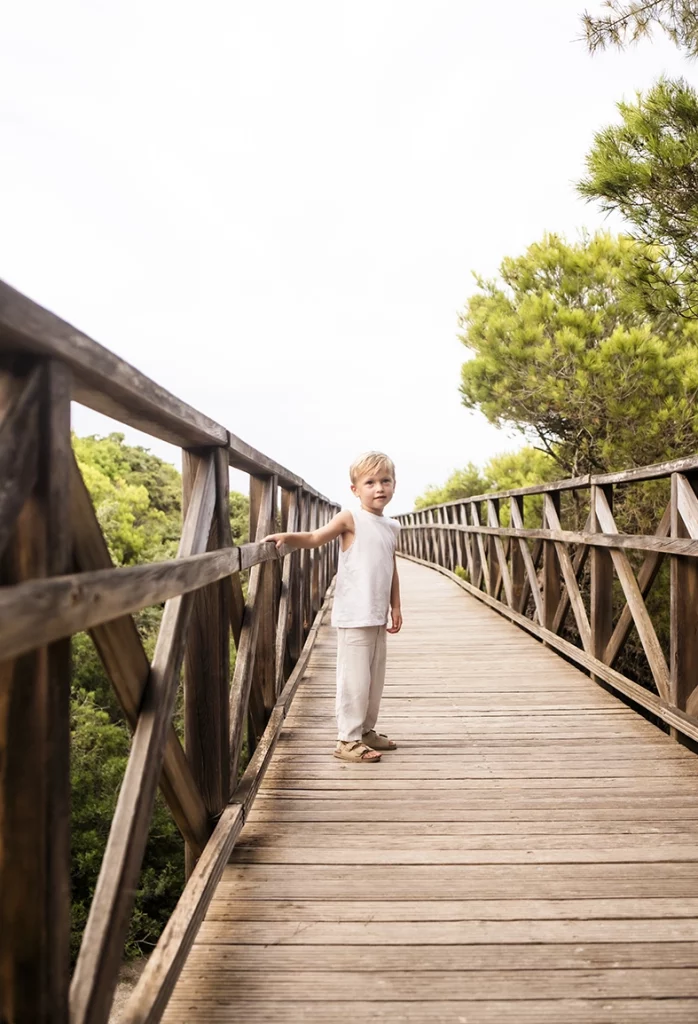 Sesión de fotos a familia en Mallorca realizada por Inma del Valle, niño caminando solo sobre una pasarela de madera rodeada de naturaleza.