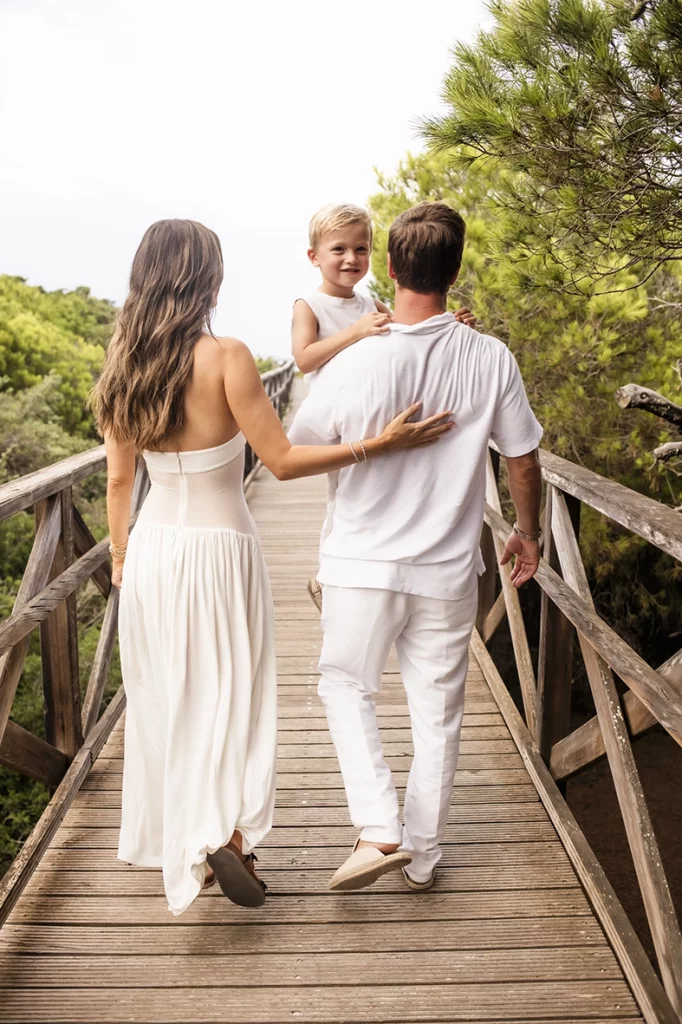 Sesión de fotos a familia en Mallorca realizada por Inma del Valle, familia caminando por una pasarela de madera hacia la playa.