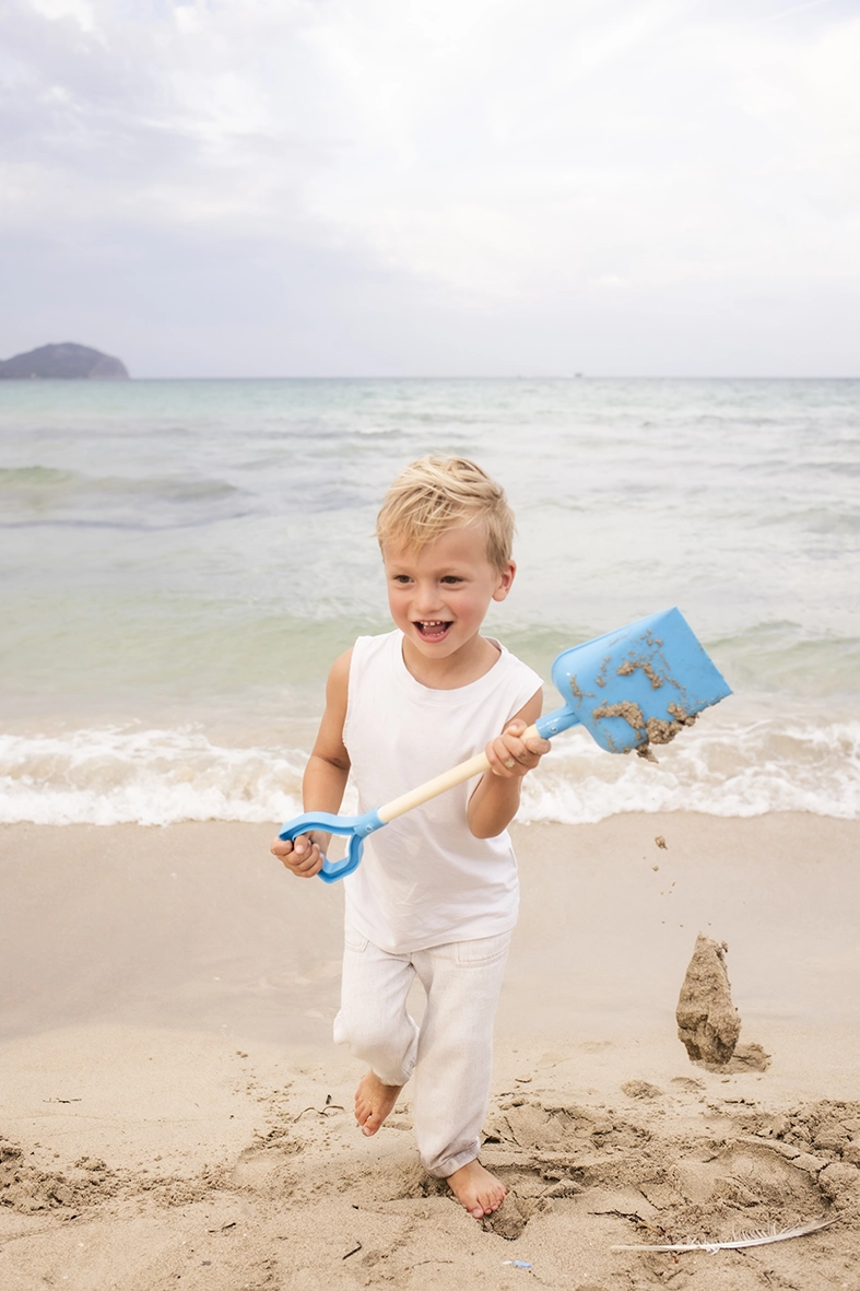 Sesión de fotos a familia en Mallorca realizada por Inma del Valle, niño jugando con una pala azul junto al mar.