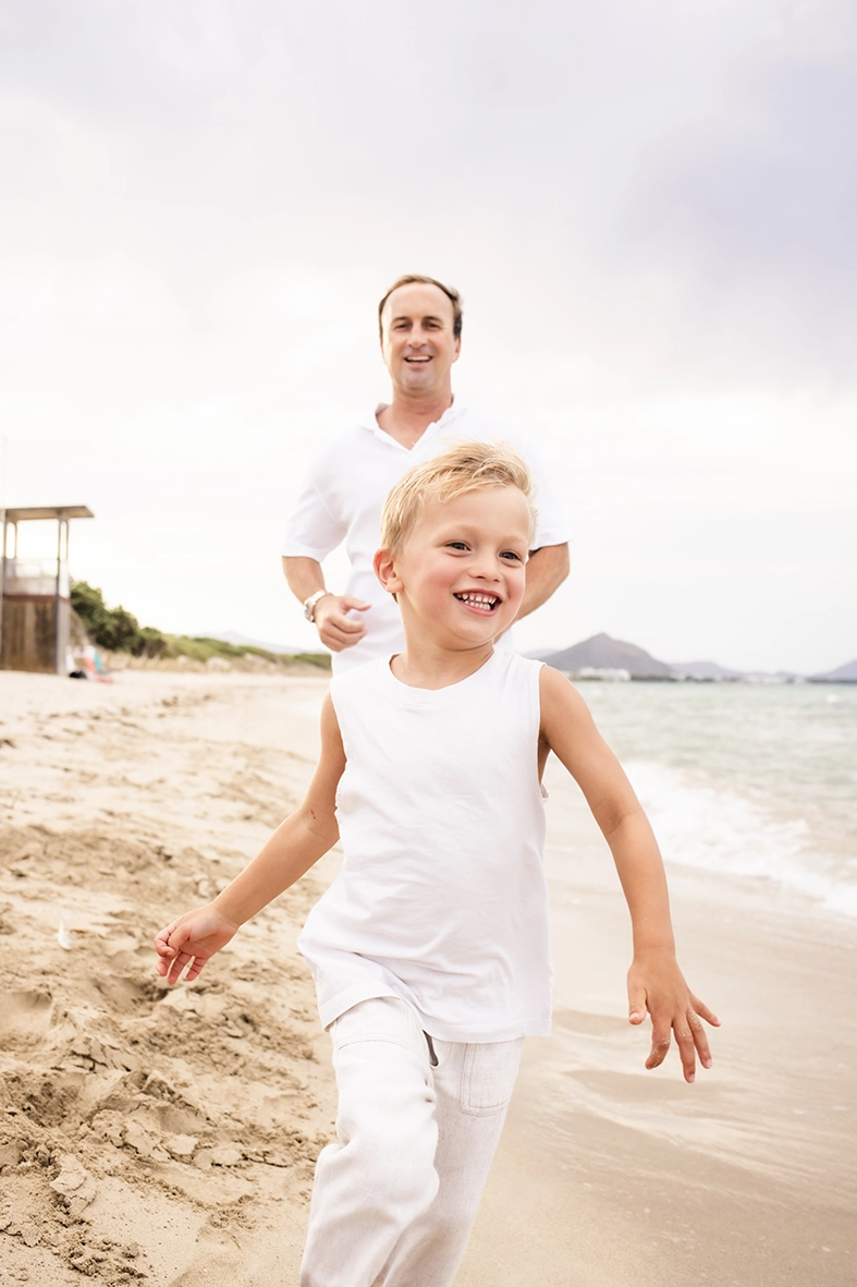 Sesión de fotos a familia en Mallorca realizada por Inma del Valle, niño corriendo feliz por la orilla mientras su padre lo sigue.
