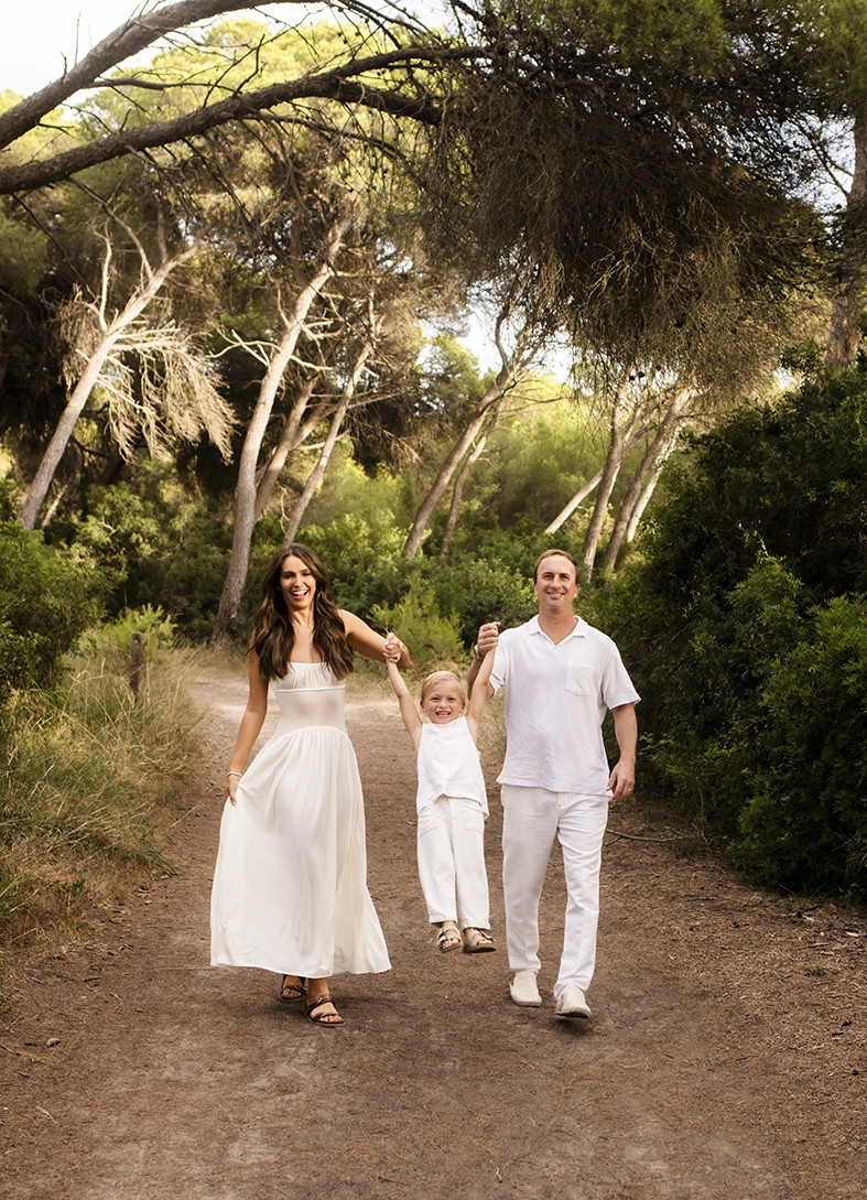 Sesión de fotos a familia en Mallorca realizada por Inma del Valle, padres caminando con su hijo entre árboles en un sendero natural.