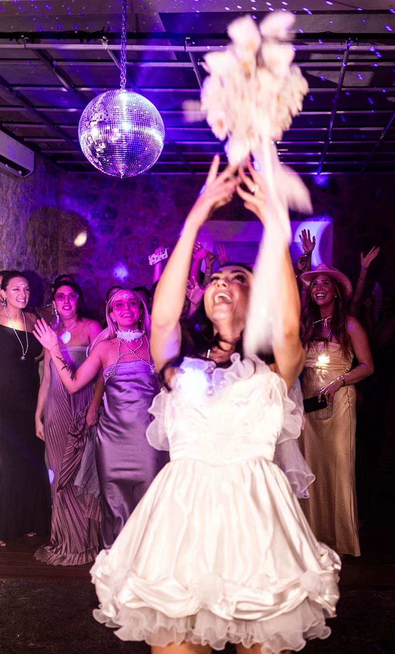 Novia lanzando el ramo con energía durante la fiesta, vestida con su vestido de novia para la fiesta. Fotografía de Inma del Valle.