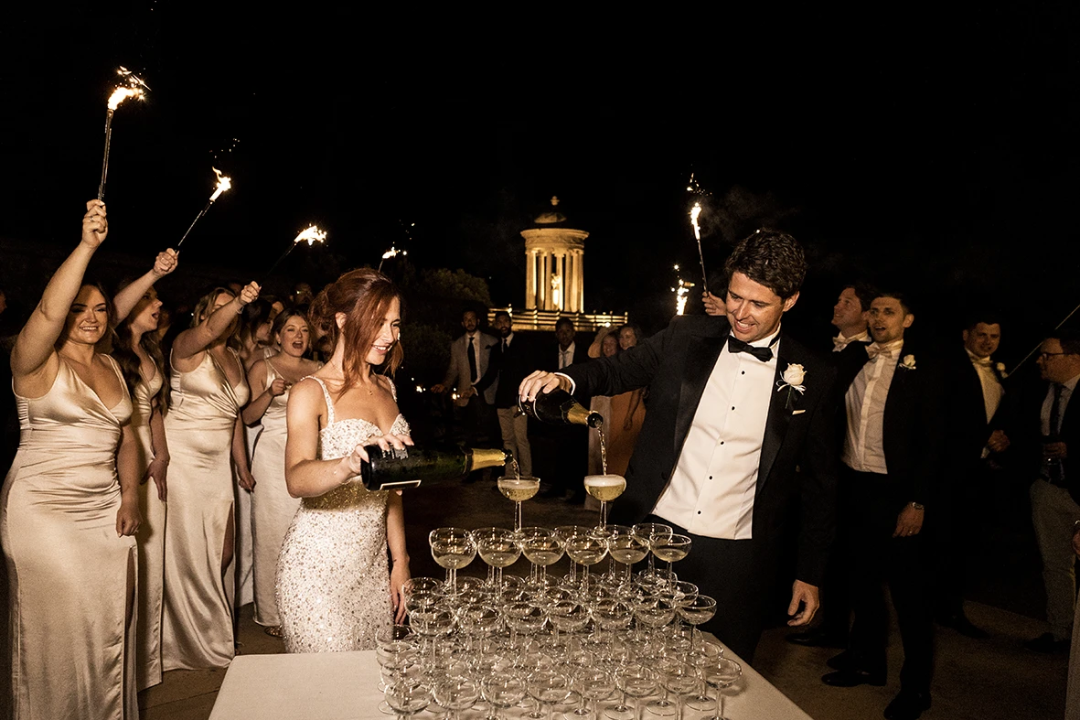 Novios sirviendo champagne en una torre de copas durante la fiesta, ella con vestido de novia para la fiesta. Fotografía de Inma del Valle.