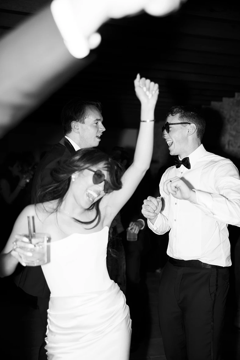 Novia bailando con gafas de sol y copa en mano, vestida con su vestido de novia para la fiesta. Fotografía de Inma del Valle.