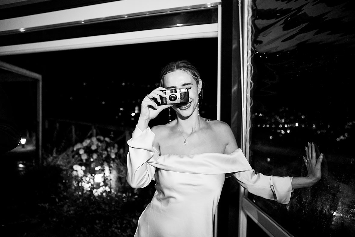 Novia brindando con una copa y sonriendo, con su vestido de novia para la fiesta. Fotografía de Inma del Valle.