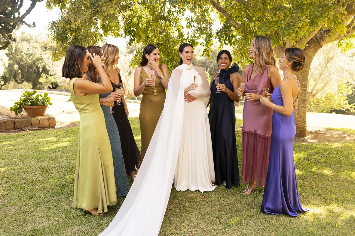 La novia sonríe rodeada de sus damas de honor bajo la sombra de un árbol – Wedding photographer in Mallorca – Inma del Valle -.
