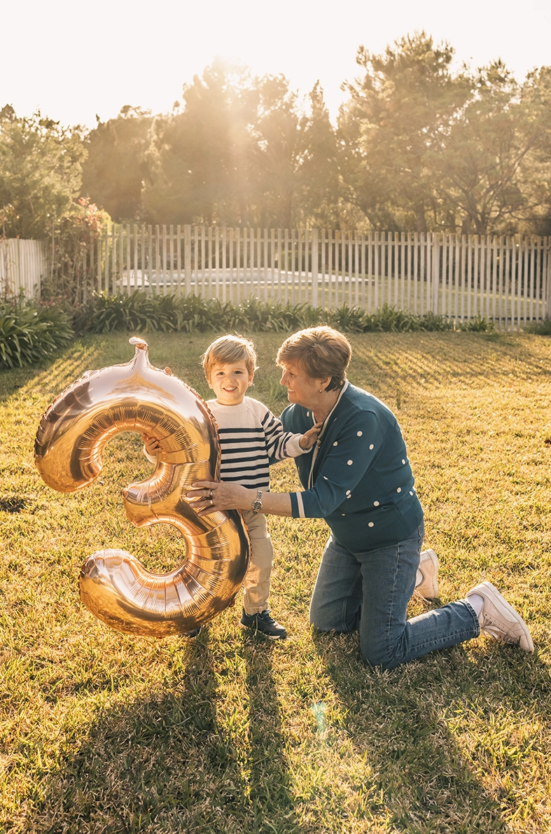 Niño y adulto jugando con un globo dorado en forma de número tres al aire libre, capturados por un fotógrafo para familias en Mallorca.