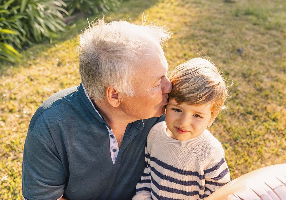 Abuelo besando a su nieto en la frente al aire libre, capturado por un fotógrafo para familias en Mallorca.
