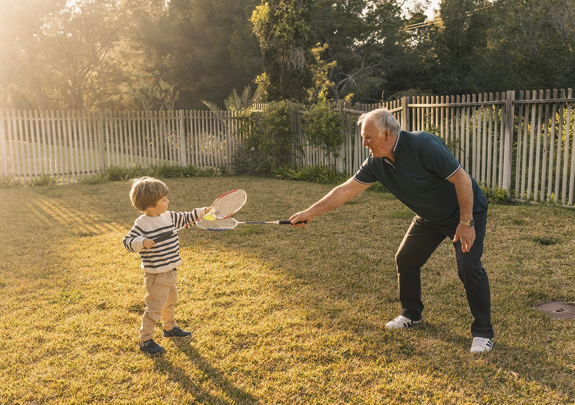 Abuelo jugando con su nieto con raquetas al aire libre al atardecer, capturado por un fotógrafo para familias en Mallorca.