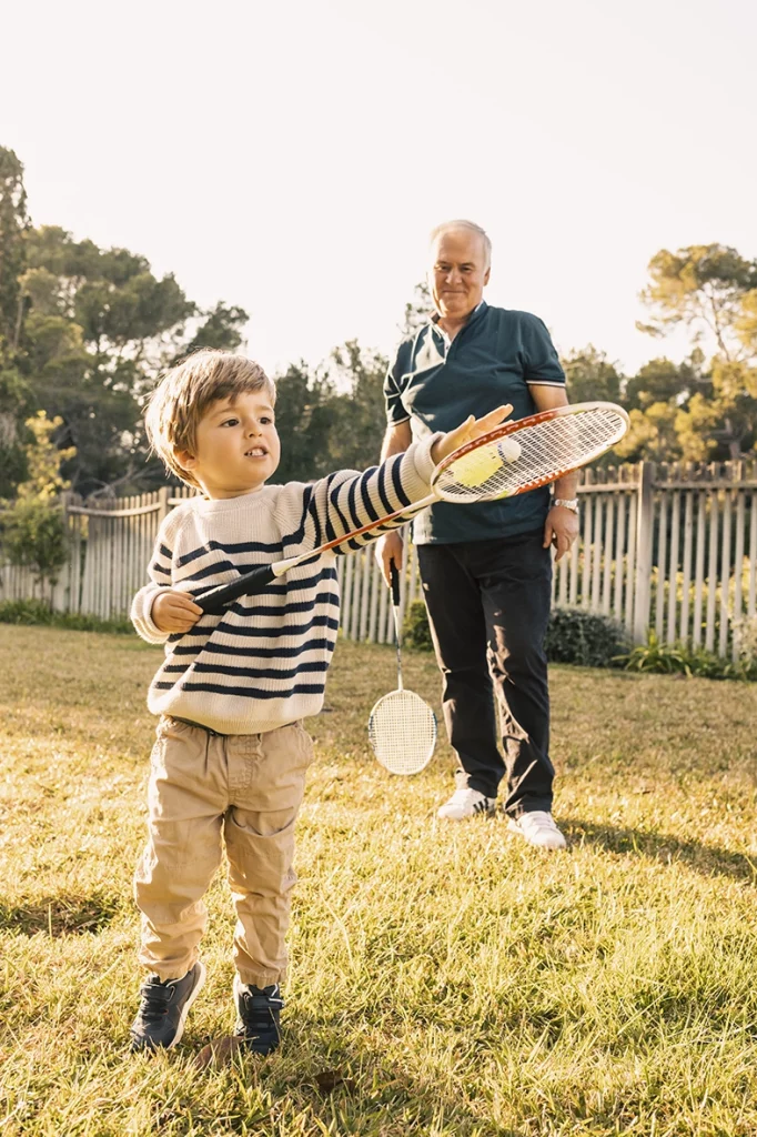 Child playing with a racket outdoors while grandfather watches, captured by a photographer for families in Mallorca.